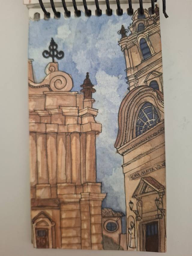 Ink and watercolor cityscape of baroque church facades in sandy browns against a blue sky, in a spiral sketchbook.